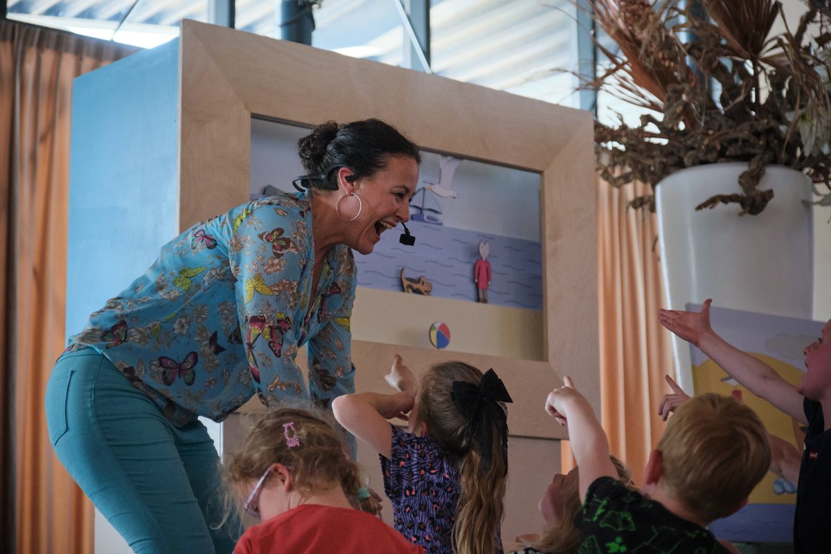 Carolien buigt bij de poppenkast naar de kinderen toe